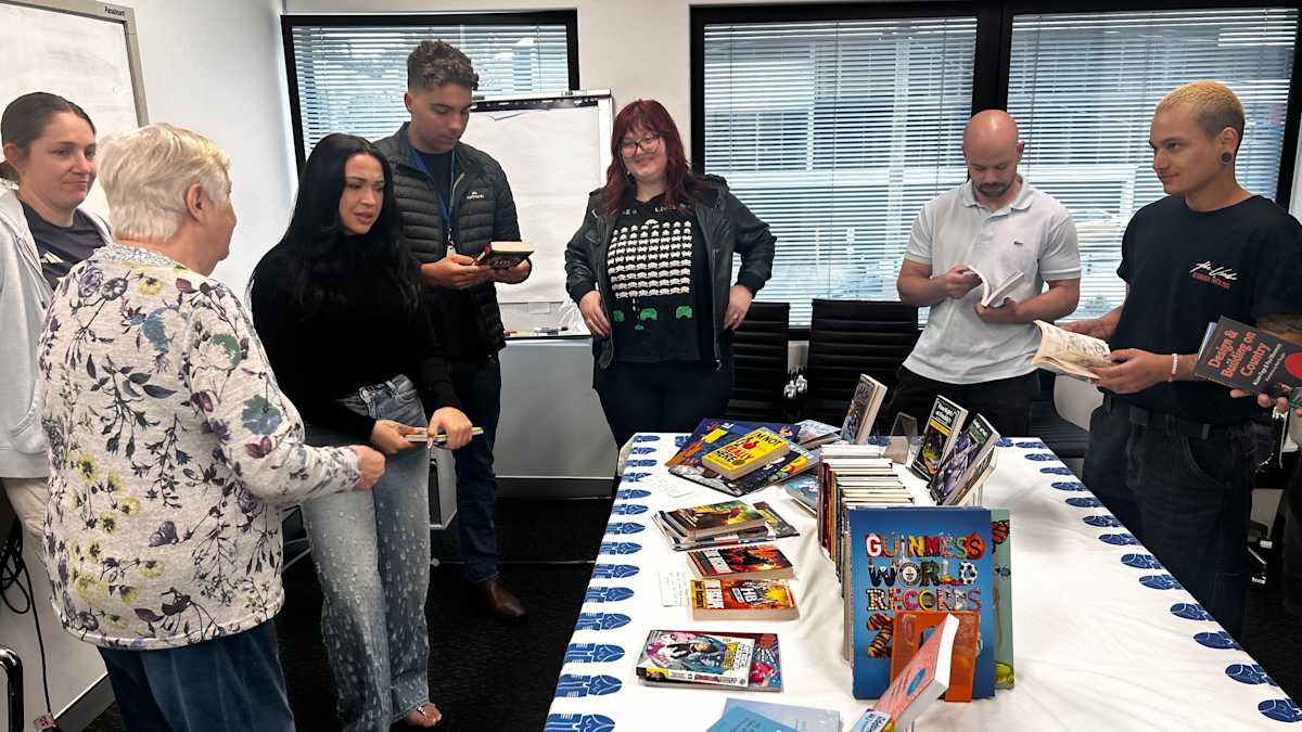 Staff gathered around a table with books on display on top of a table cloth with the the Children’s Book Council of Australia logo.