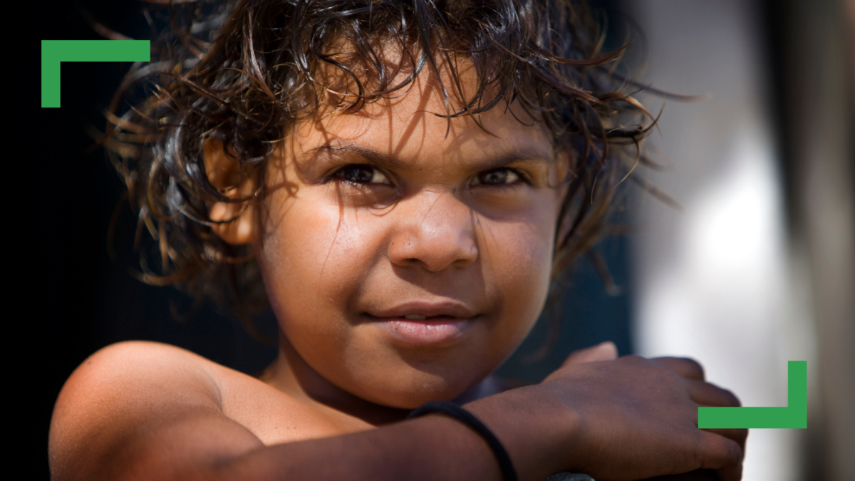 Close up of a young Aboriginal boy with curly brown hair smiling at the camera.