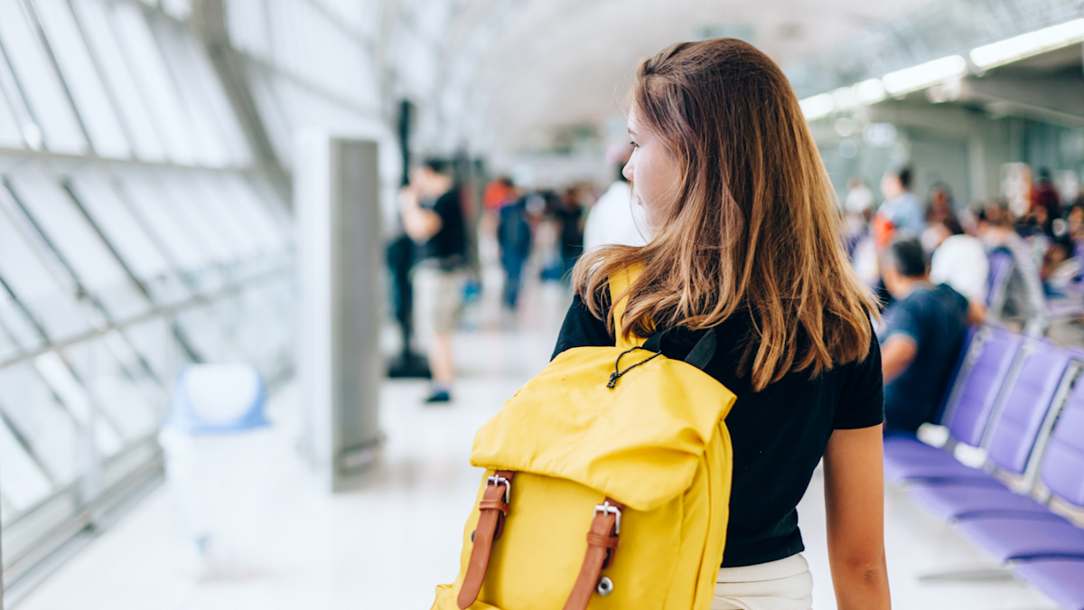 83 Teenage girl with a yellow backpack walking through the airport.