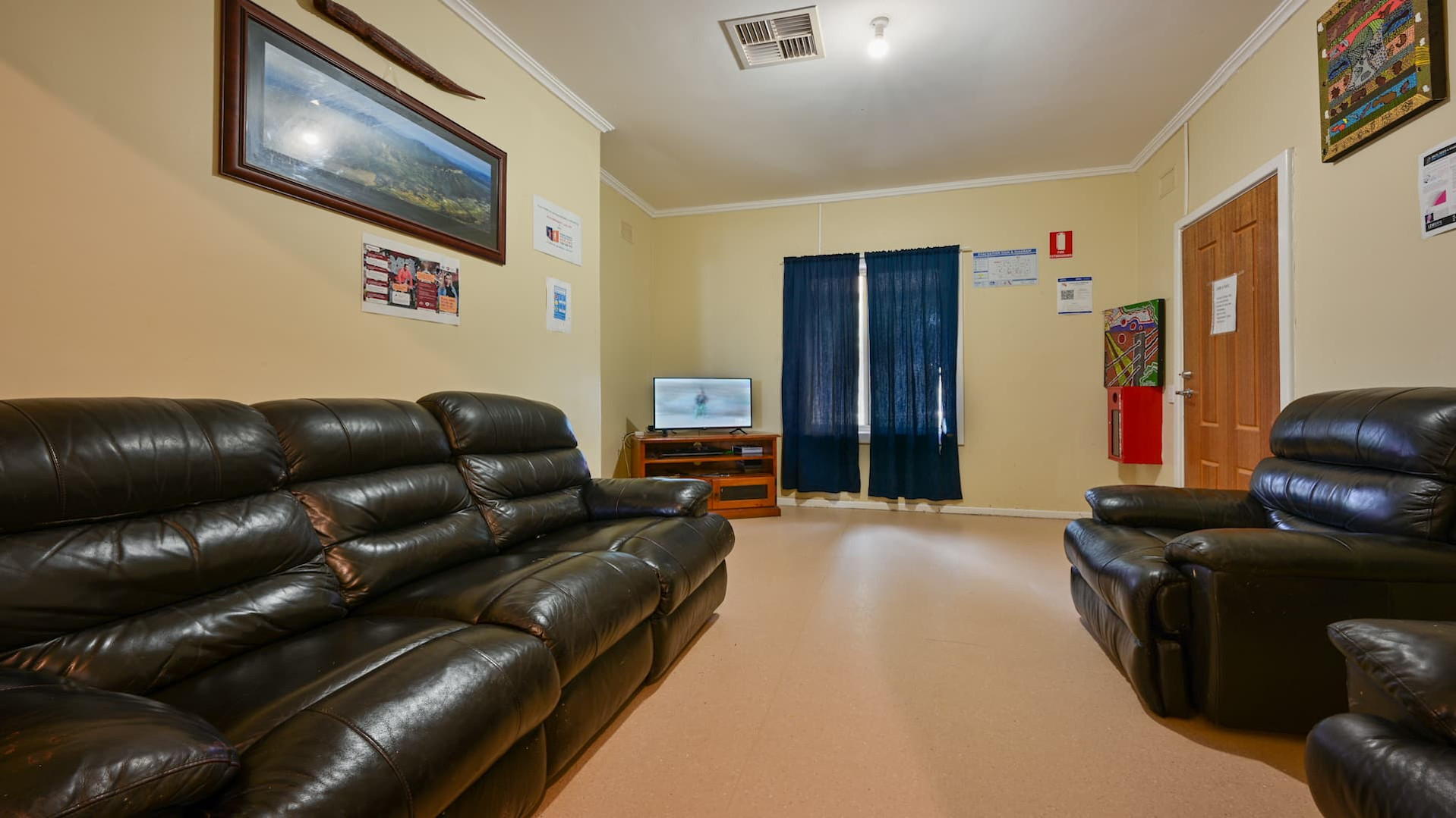 Simple living room with a light grey two-seater sofa, wooden coffee table and TV unit, wall art, and a striped rug, with dark blue curtains covering the windows.