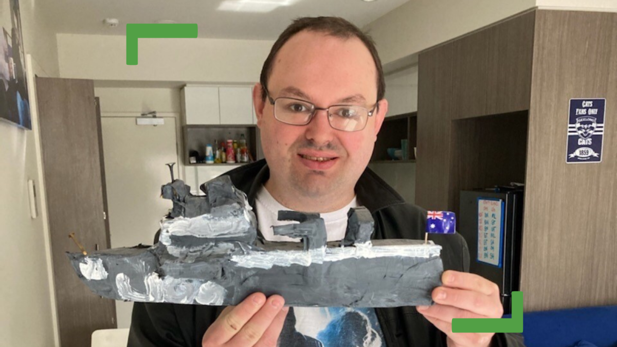 Will wearing glasses and smiling at the camera while holding a painted model ship.