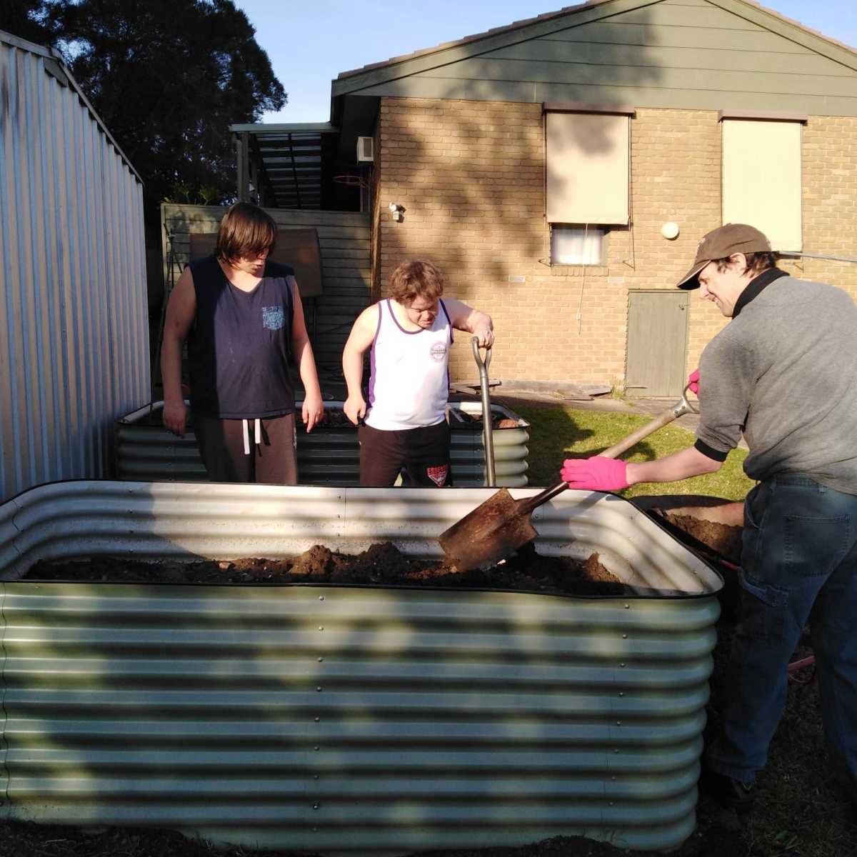 Three people standing around a raised garden bed with gardening tools.