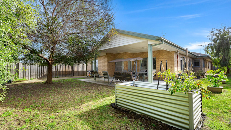 Mount Waverly home backyard. Grass, planter box and yellow brick home with trees surrounding.