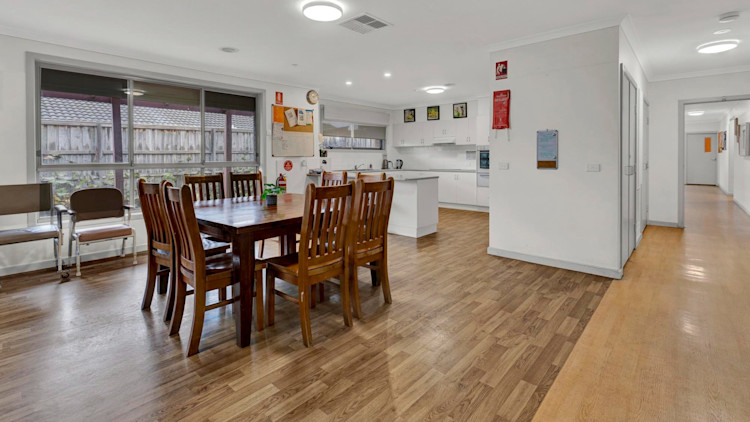 Light-filled open kitchen and dining space with wooden dining table, eight chairs, and sliding doors leading to the outdoor area.