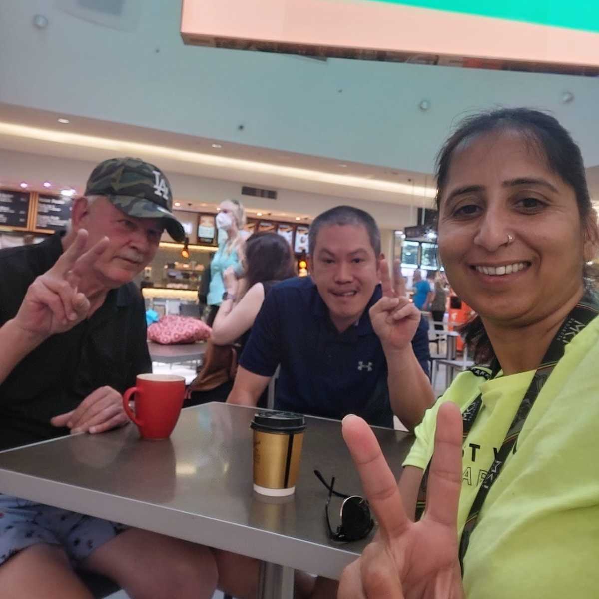 Two of the housemates with a support worker having coffee in a shopping centre.