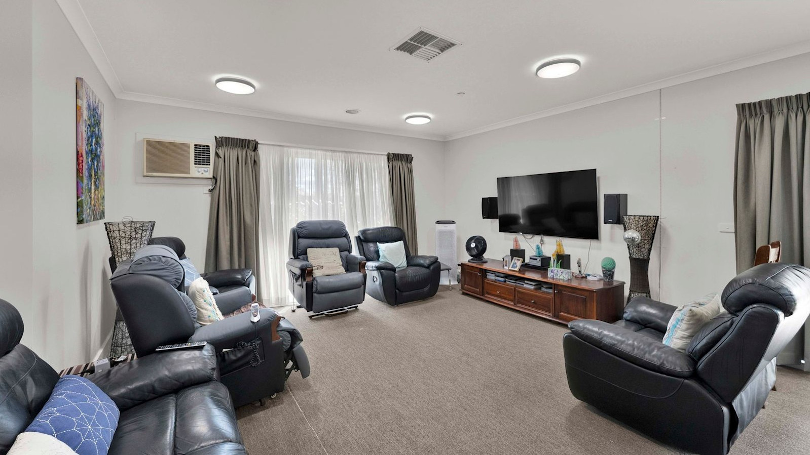 Comfortable lounge area with black recliner chairs, wall-mounted television, and natural light from large windows.