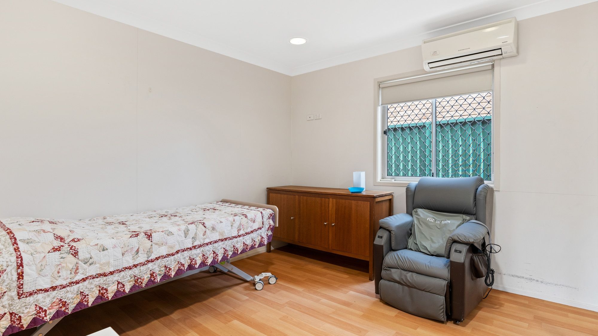 Bedroom with single bed, armchair, bedside table, wooden cabinet and air-conditioner.