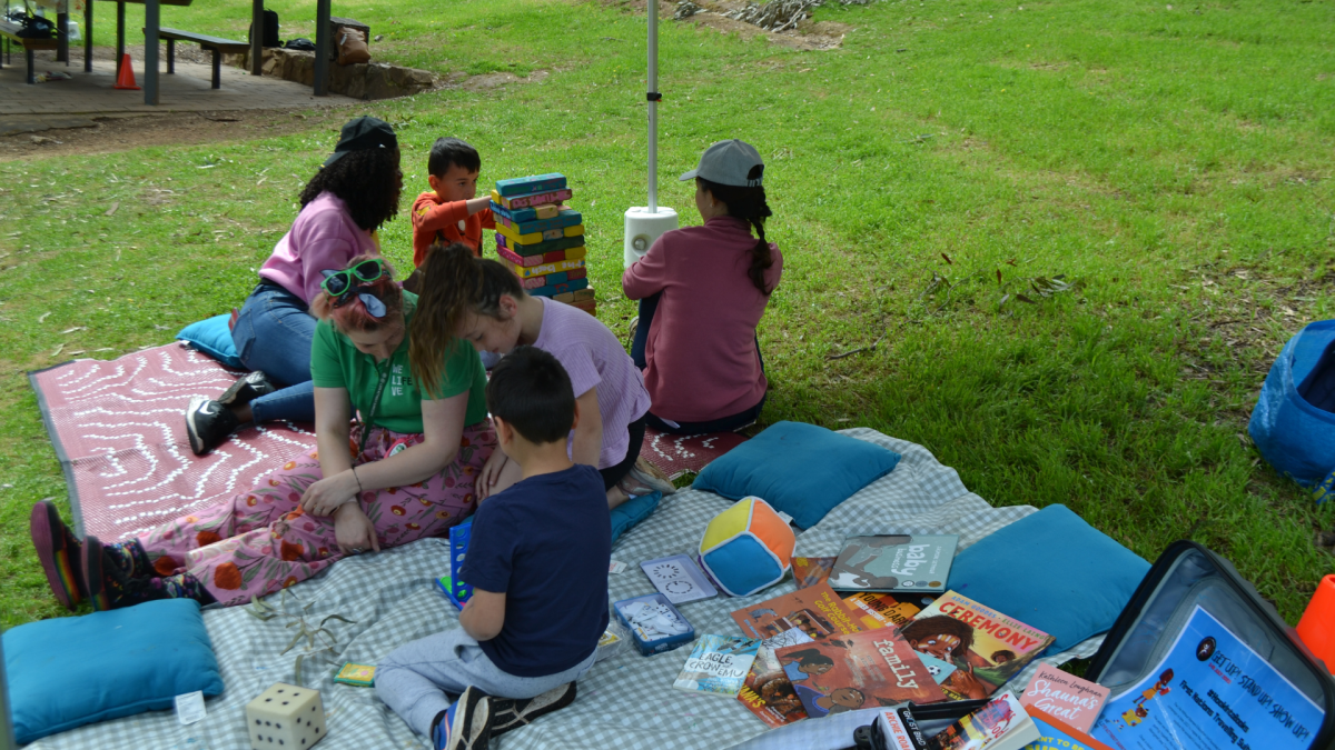 People spread out on a picnic blanket reading books.
