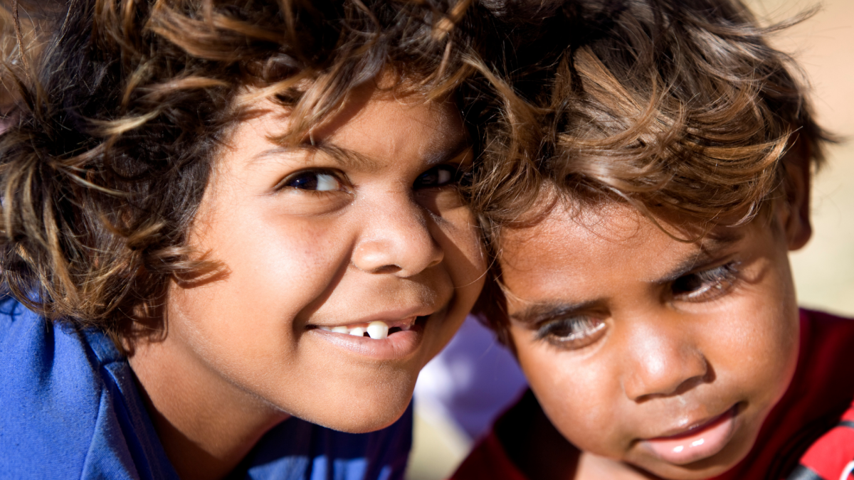 Close up of two Aboriginal children smiling at the camera with their heads together