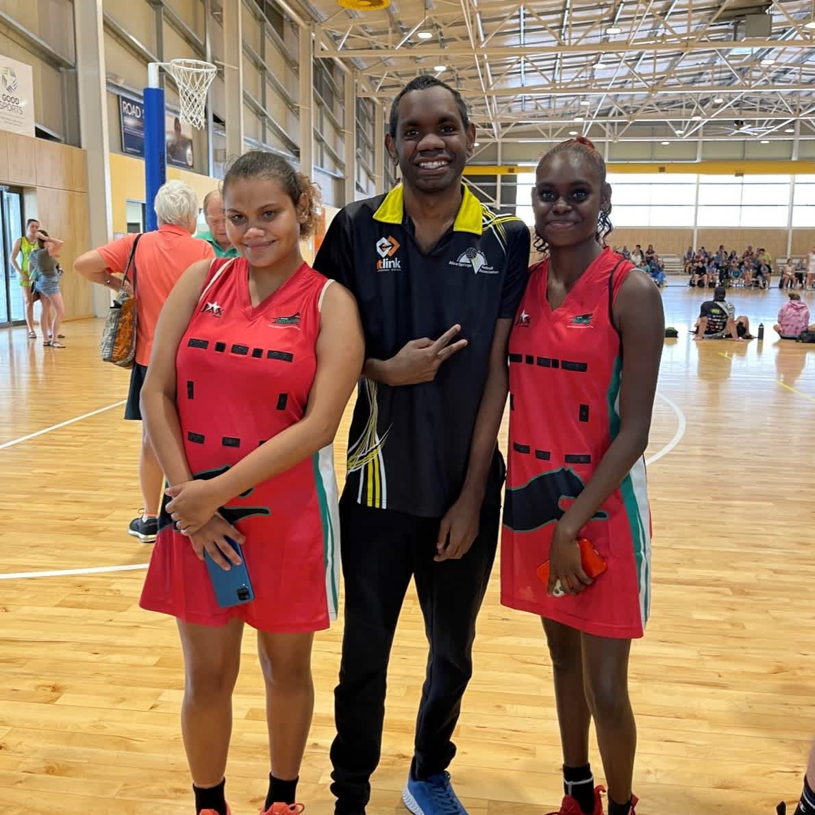 Micky standing with two female teammates on the netball court.