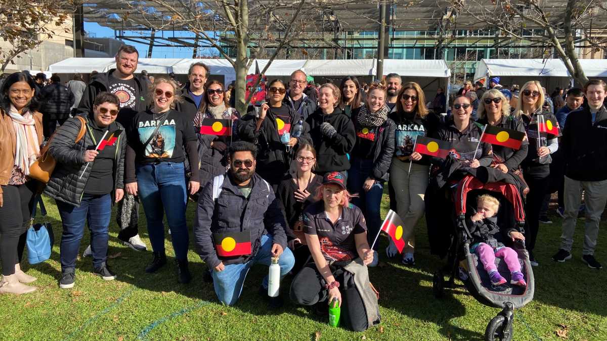 Life Without Barriers staff stand together in a large group outdoors. Many are holding the Aboriginal flag.