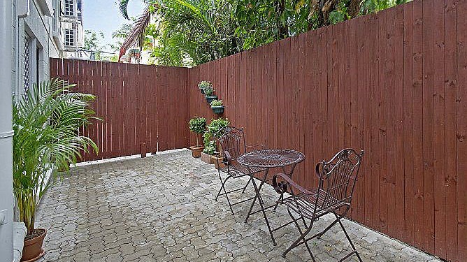 Paved fenced courtyard with an outdoor set and plants. 