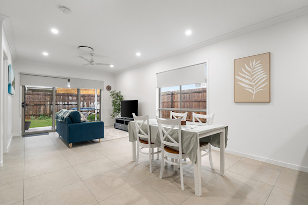 Light-filled dining space with white table and chairs beside large windows and wall art.