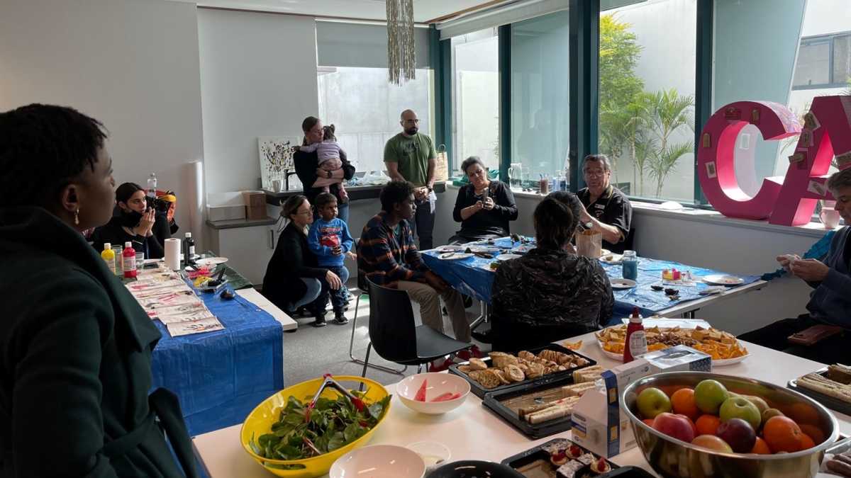 A group of people sit in a decorated room around tables listening to a man tell a story.