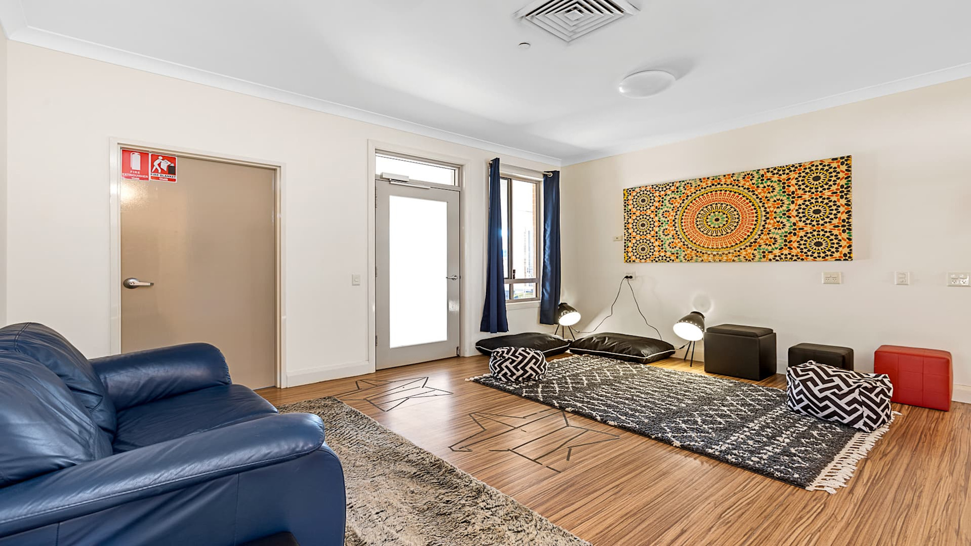 Second living space with floor rug, cushions and lounge chair facing orange abstract artwork.