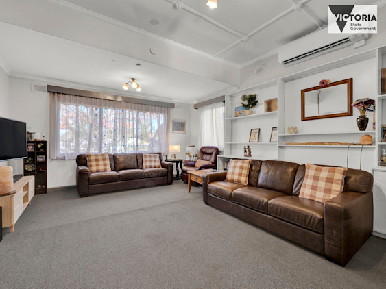 Spacious living room with two brown leather sofas, checkered cushions, built-in shelving, and large front window with sheer curtains.