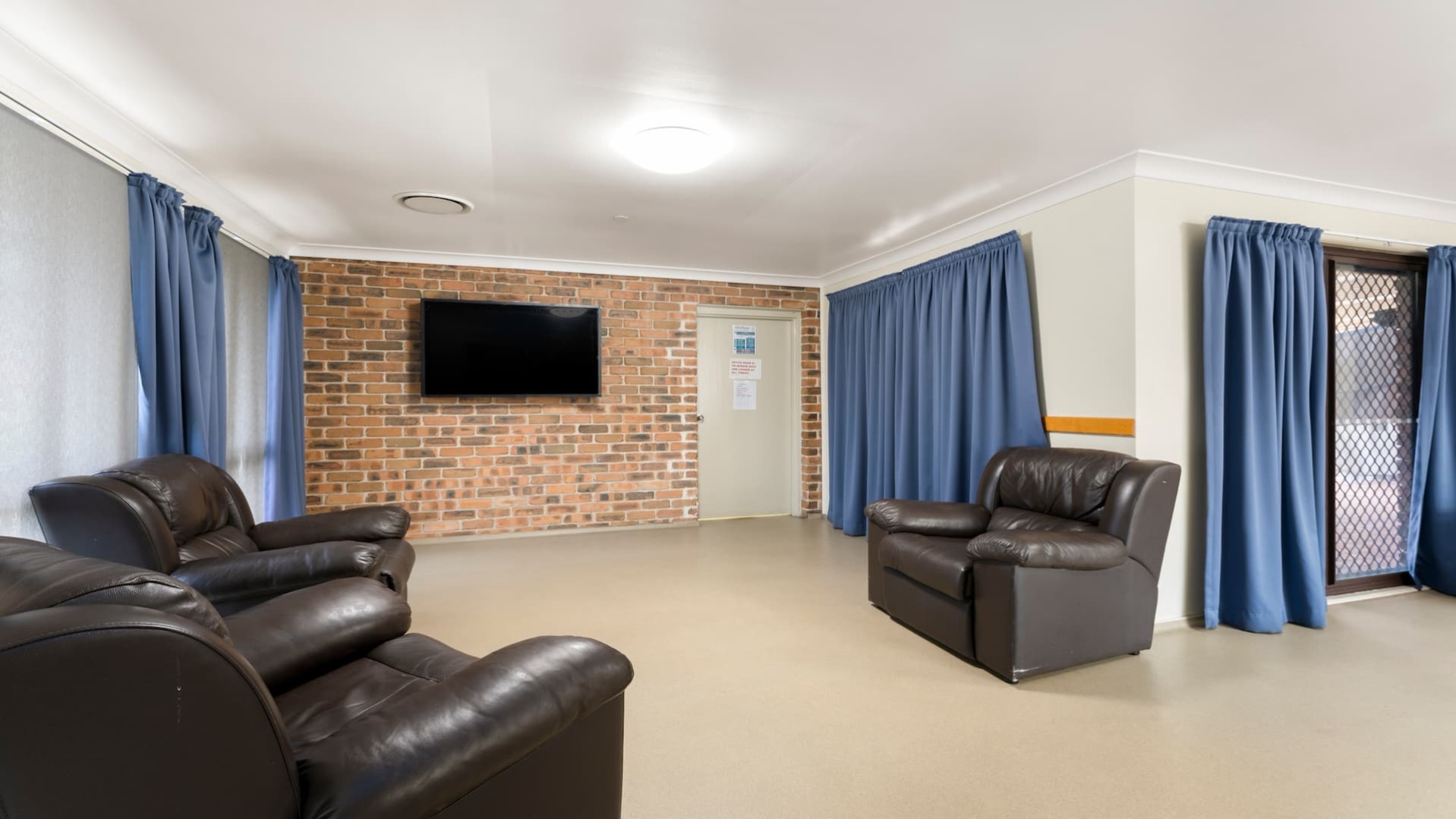 Lounge room with black armchairs and a TV mounted on the wall.