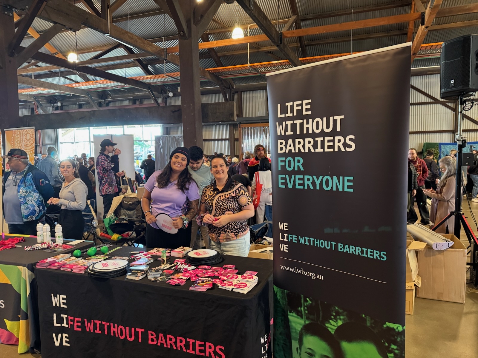 Chloe Appo, Program Assistant and Kirsty Burley, Child and Family Practitioner, standing behind the Life Without Barriers booth at the Toowoomba NAIDOC Expo.