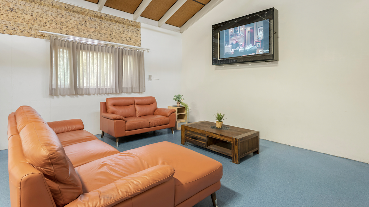 Lounge area with two light brown couches, a TV mounted on the wall, a wooden coffee table and a small stand with plants.