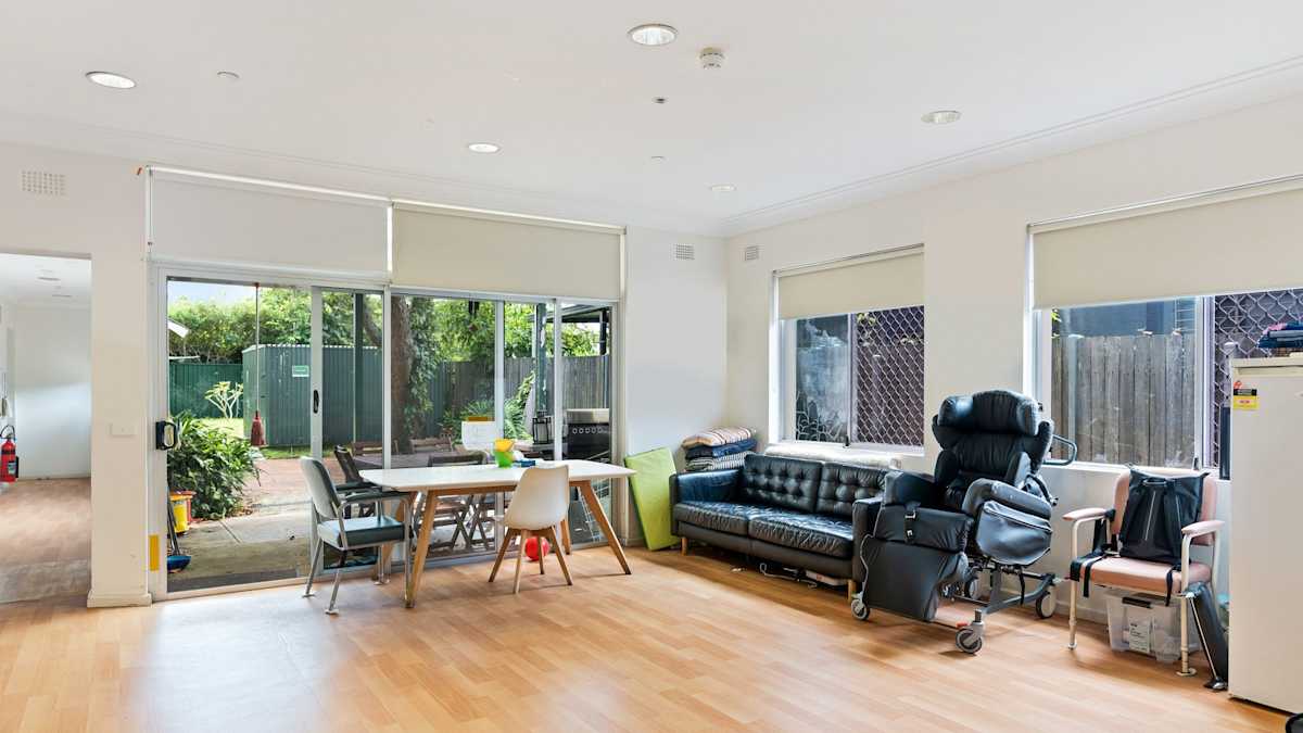 Spacious loungeroom surrounded with windows, hard flooring and dining table and chairs near sliding door to outdoor patio.