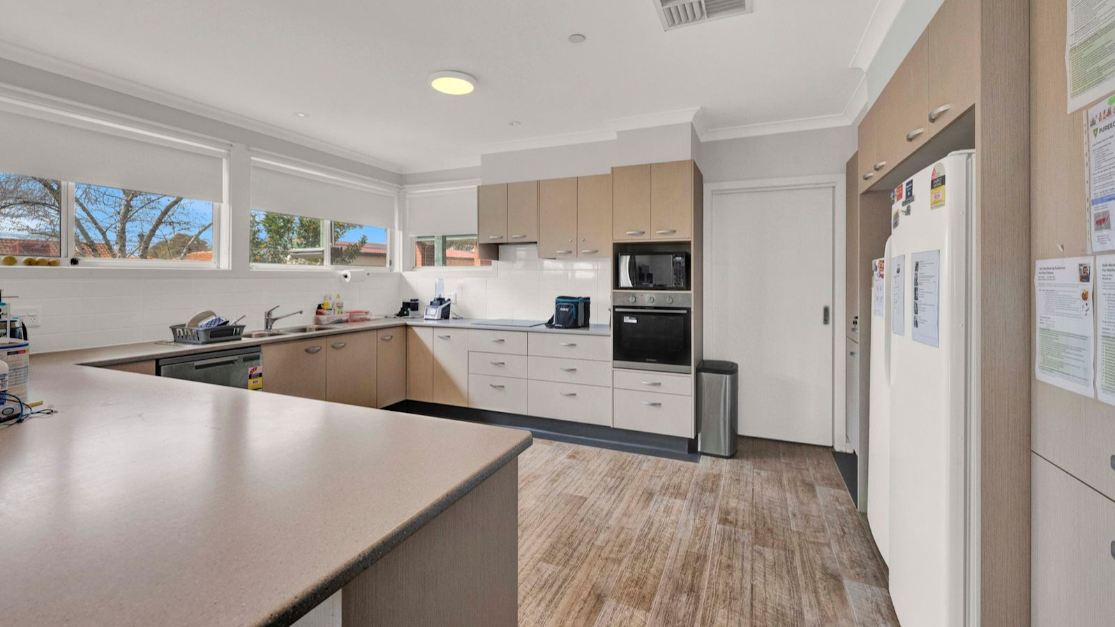 Modern kitchen with U-shaped bench, overhead cabinets, oven, microwave, and large refrigerator.