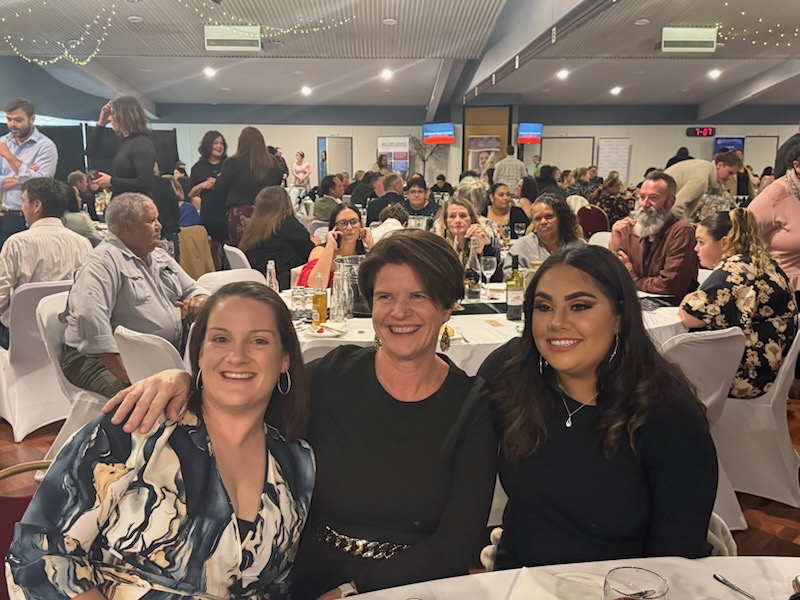 Kirsty Burley, Child and Family Practitioner, Karen Smith, Youth Work Coordinator, and Chloe Appo, Program Assistant, sitting at a table at the gala dinner, smiling at the camera.