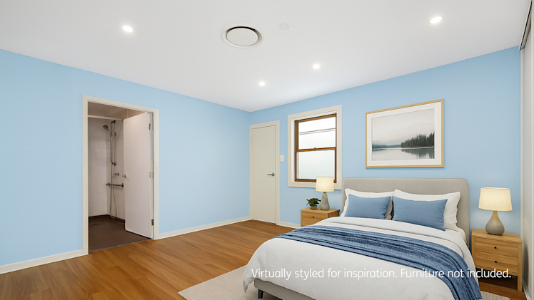 Spacious bedroom with light blue walls, ensuite bathroom, wooden floors, and a bed with blue accent pillows and decor.