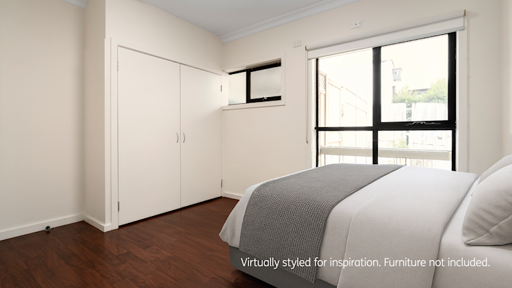 Bright bedroom with a neatly made bed in white and grey linens, built-in wardrobe, and large window with natural light and garden views.
