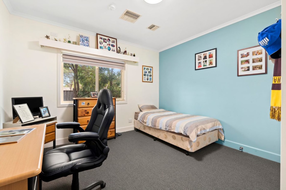 --Bedroom with a desk, TV, chest of drawers and a single bed against a light blue wall.--