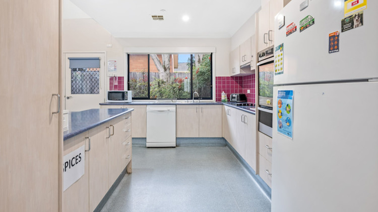 Modern kitchen featuring light cabinetry, red tiles, blue benches, and window views to the backyard.