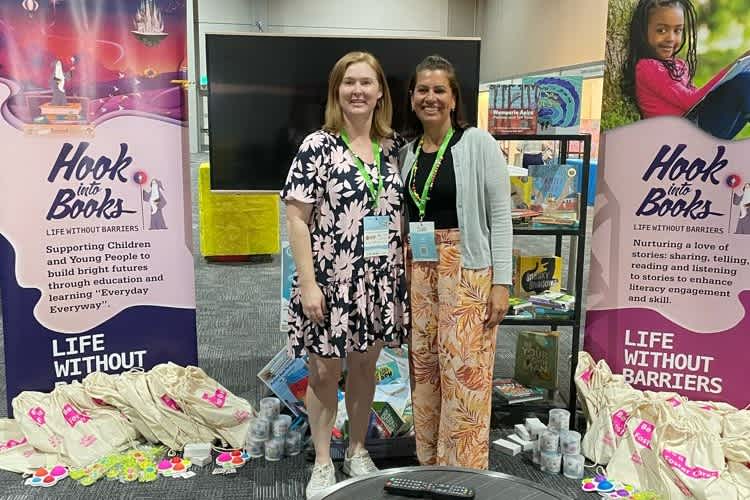 Megan and Clea sharing our Hook into Books with attendees. Standing in front of two Hook into Books banners.