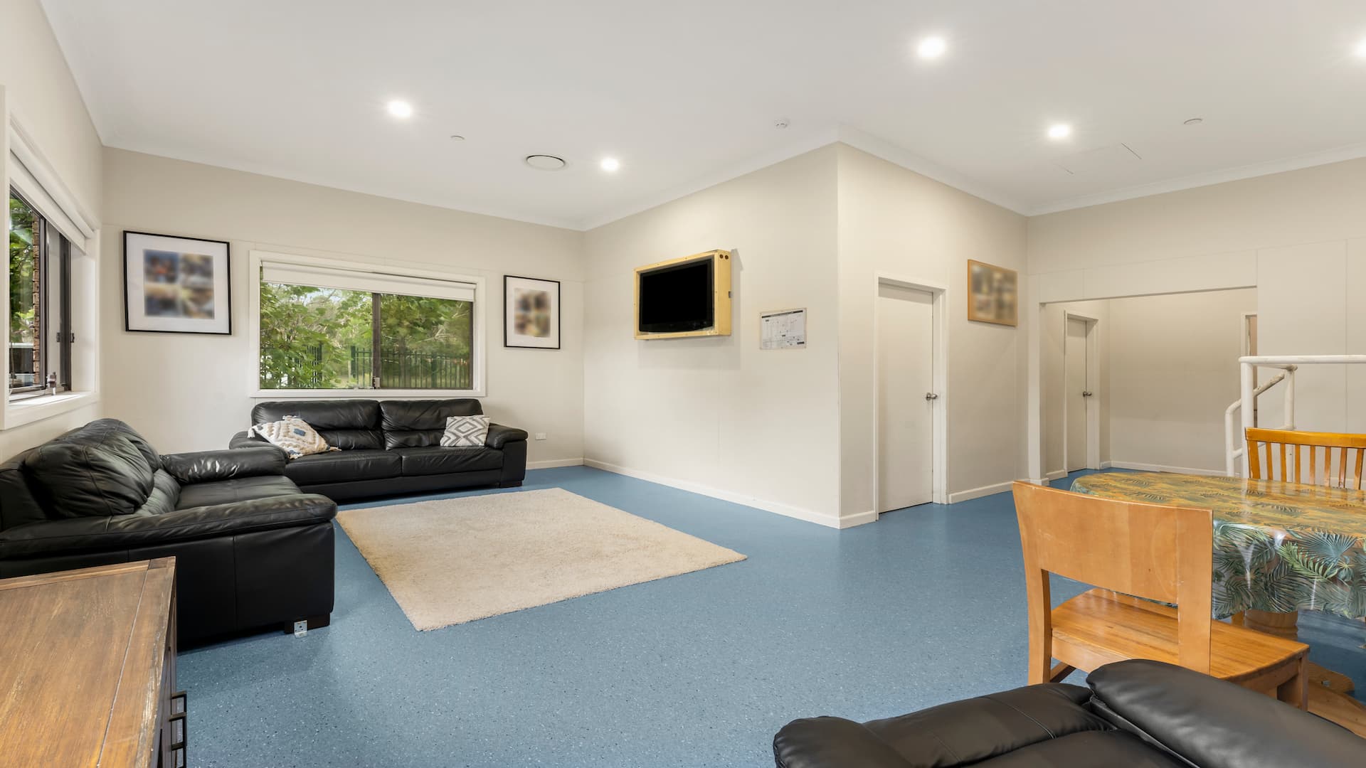 Lounge area with two black couches, an arm chair, a wall-mounted TV, and a table with chairs.