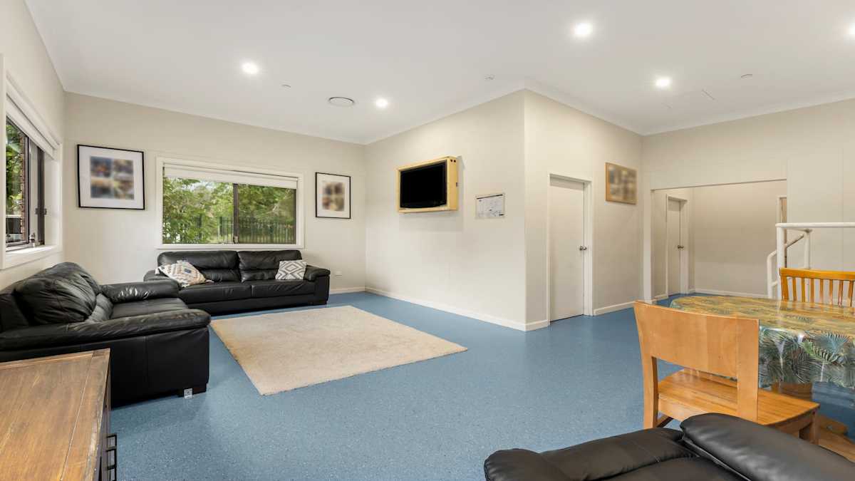 Lounge area with two black couches, an arm chair, a wall-mounted TV, and a table with chairs.