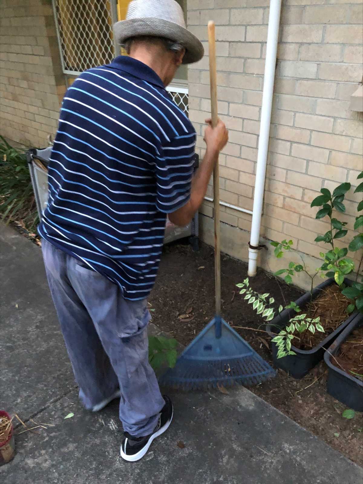Simon holding a rake, gardening outside.