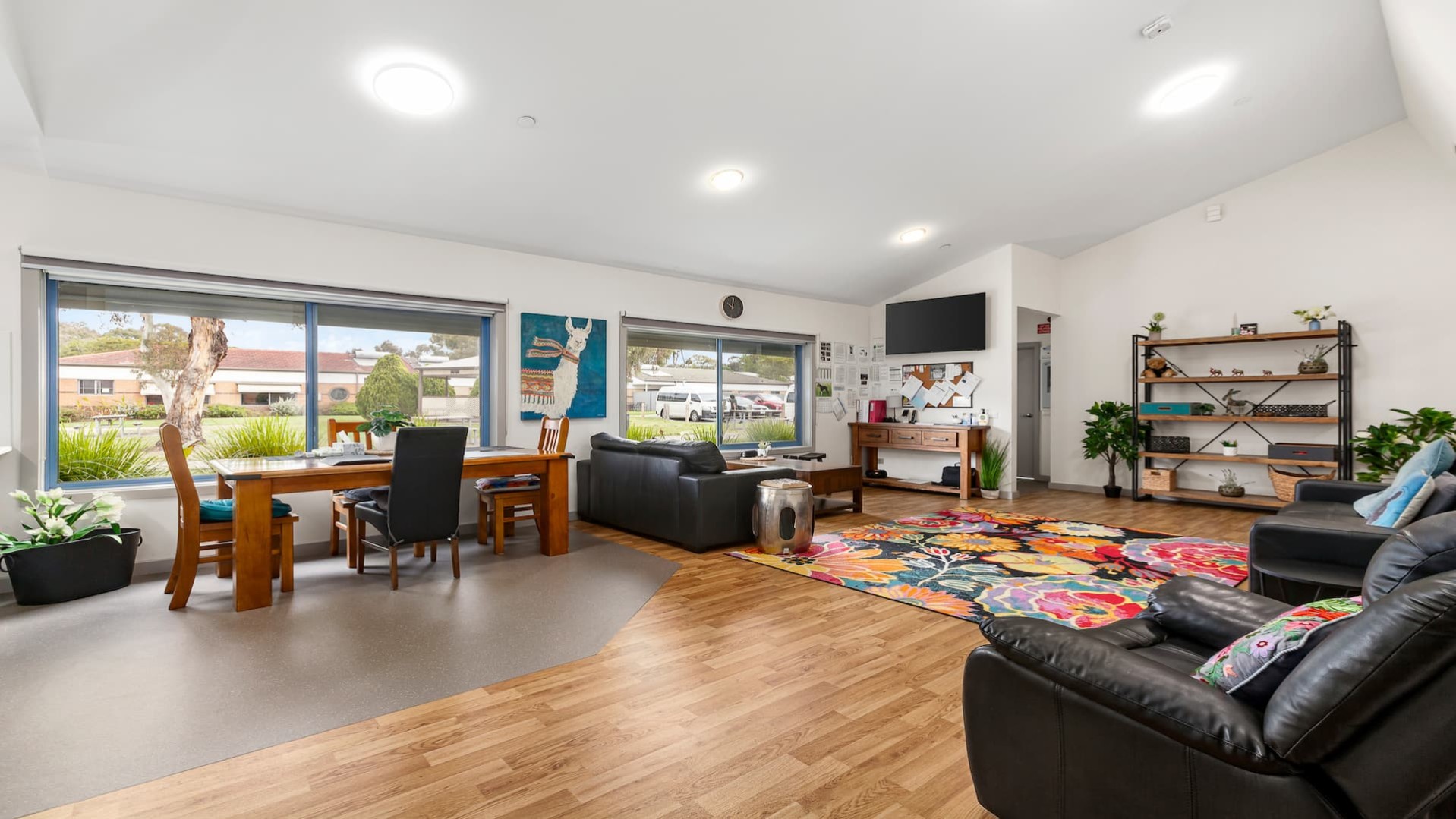 open plan lounge and dining area with dinner table in front of large picture window, colourful rug and leather couches.