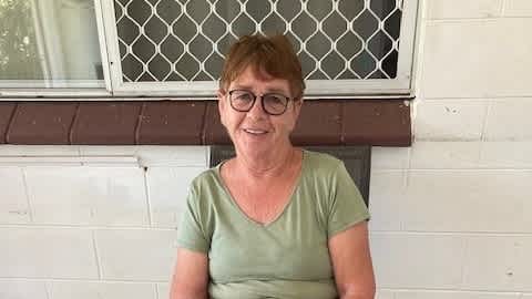 Norma sitting in a chair wearing a green t-shirt and glasses.