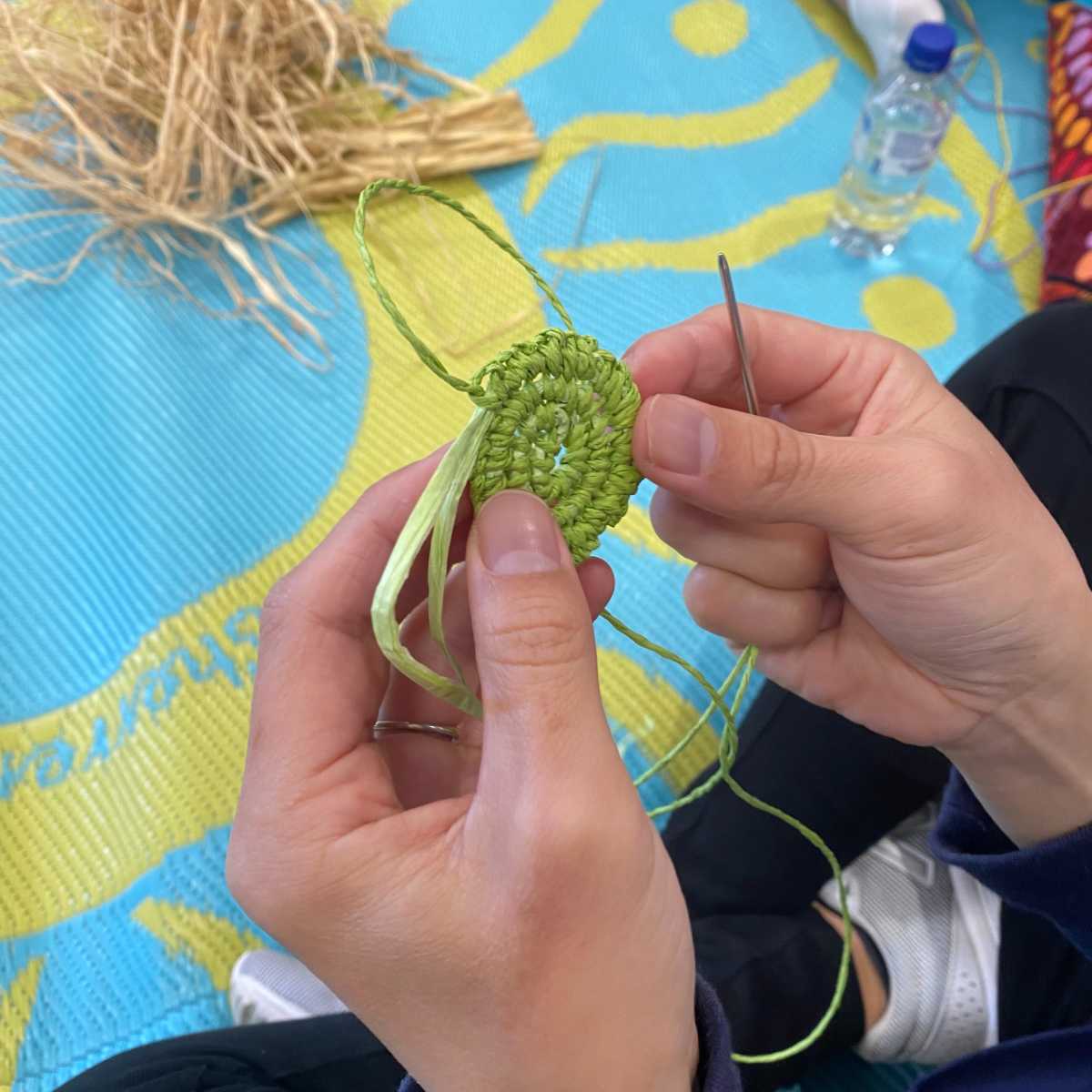 Close up of a person's hands holding a needle and a green woven spiral.