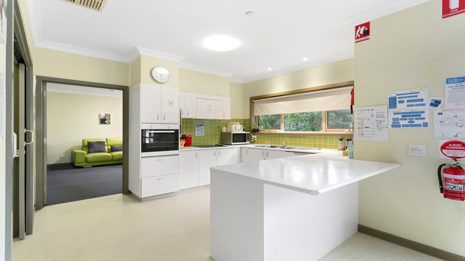 Open plan kitchen with white benchtops and green splash back.  Includes oven, microwave and stove top.