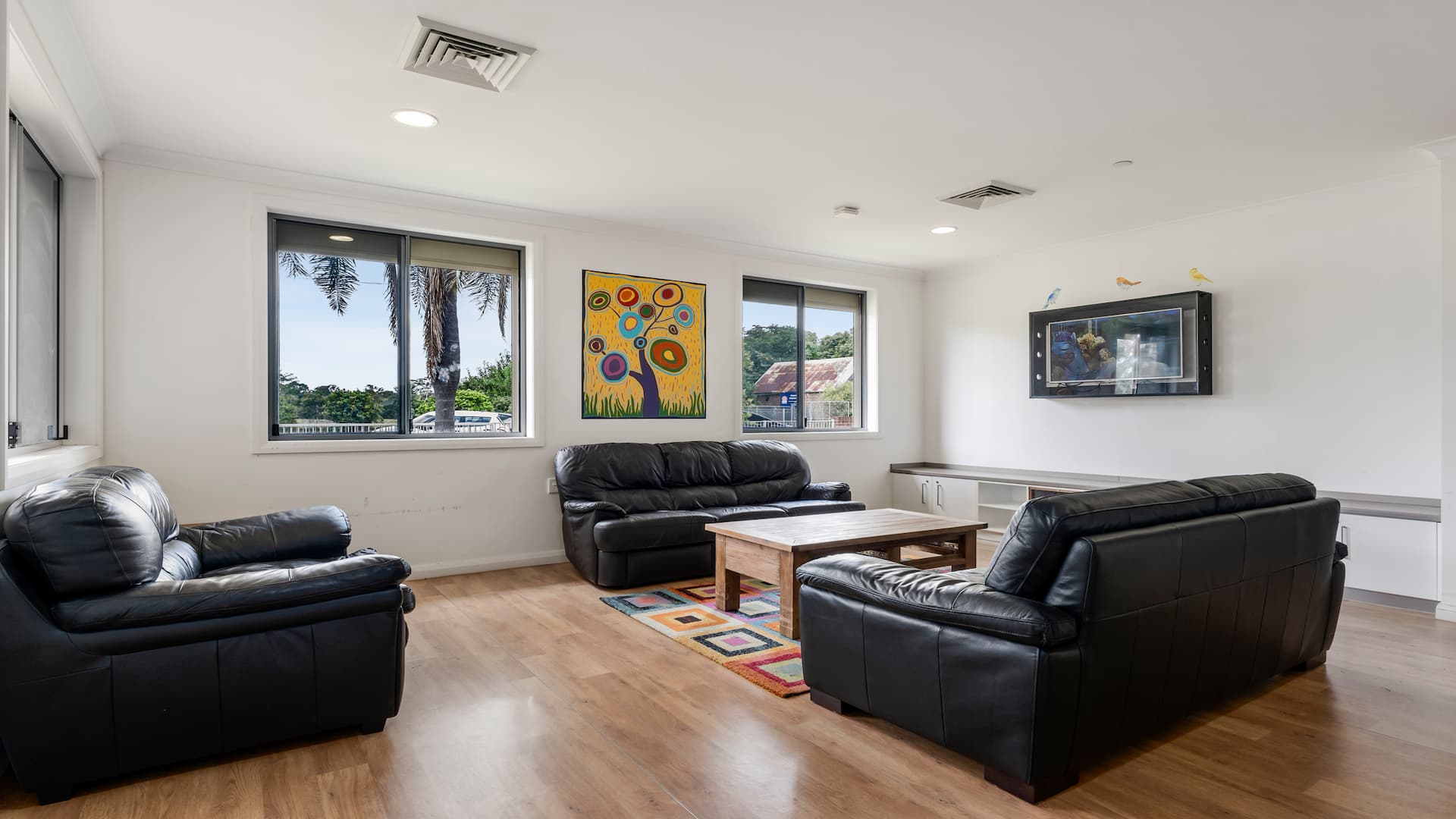 Lounge room with two black couches, a black armchair, a wooden coffee table and a wall-mounted TV.