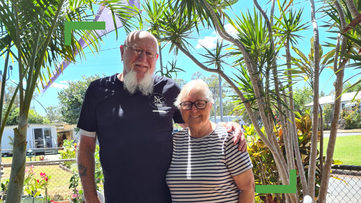 Ray and Maureen standing outside in their garden. Ray is wearing a dark blue t-shirt and Maureen is wearing a white and blue striped t-shirt.