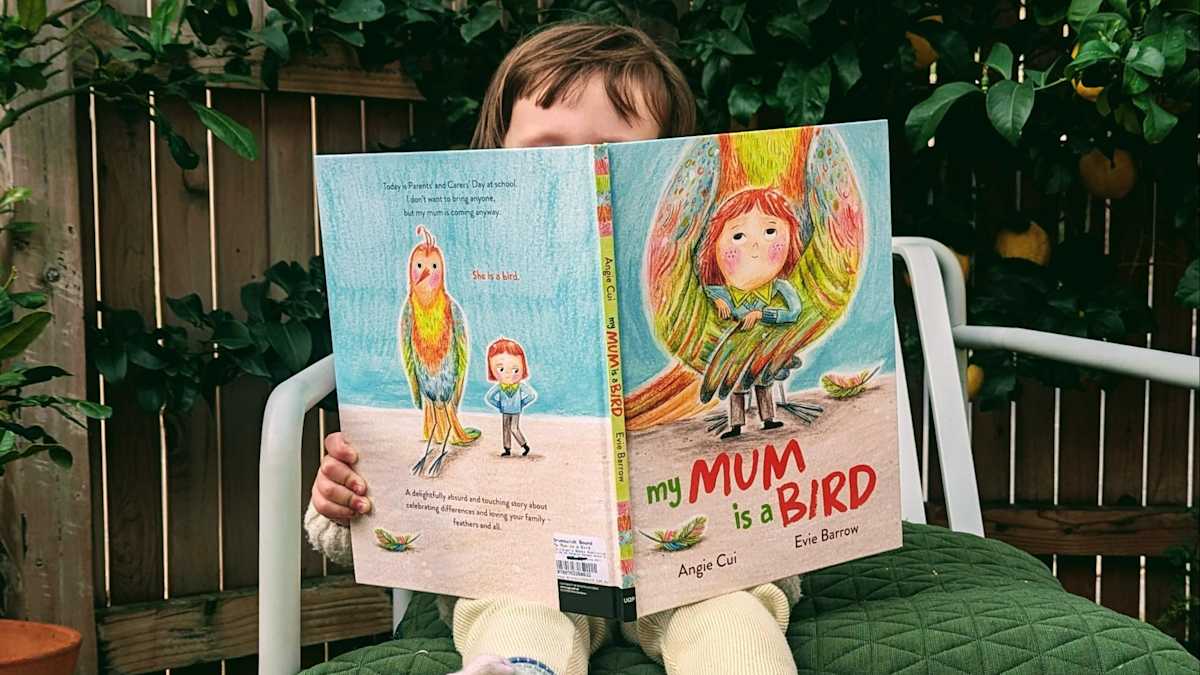 A child sits on a chair outdoors, holding a picture book open in front of them.