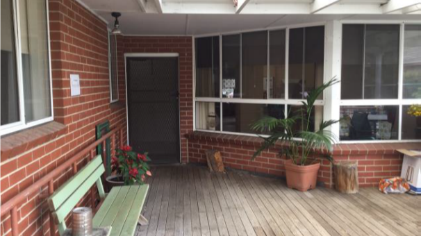 Red brick home, wooden deck, white rafters, entry way. 