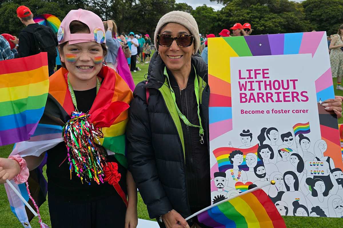 A young person and Life Without Barriers foster carer, Rana, wearing rainbows and holding a Life Without Barriers banner at the Midsumma Pride March.