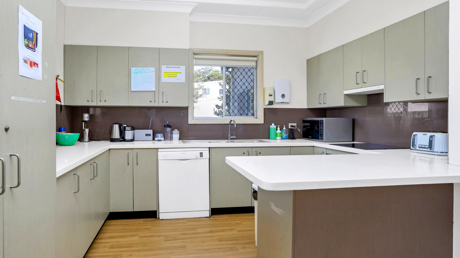 Modern kitchen with light cabinetry, white benchtops, dishwasher, microwave, and ample storage space.