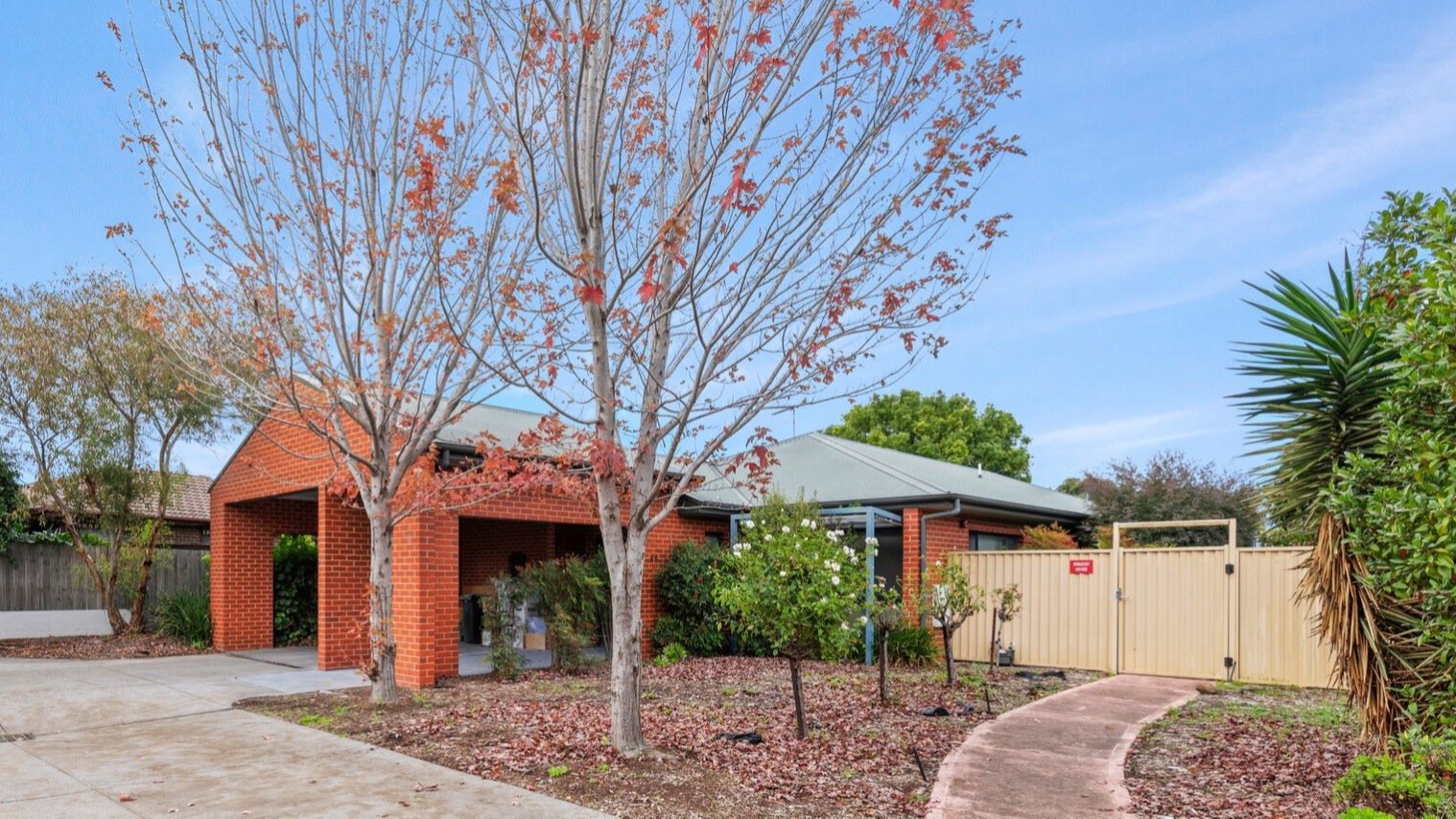 --Front of house with carport, two trees and a pathway leading towards a gate--