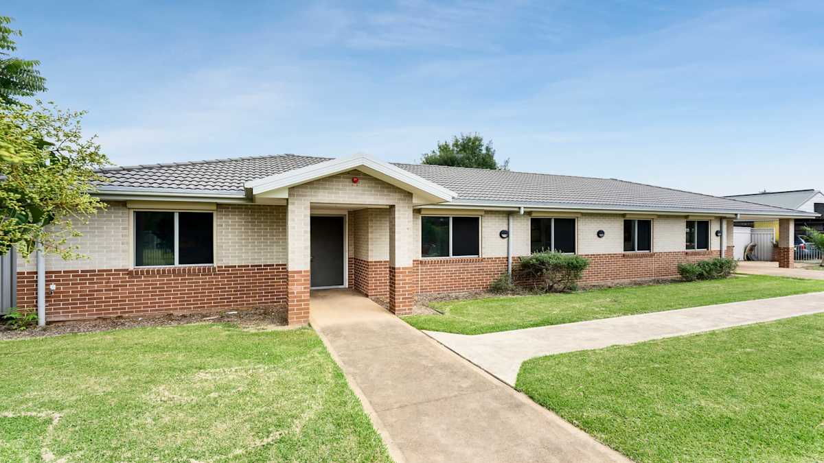 House with a brick facade and a concrete path leading to the front door with grassed areas on either side.