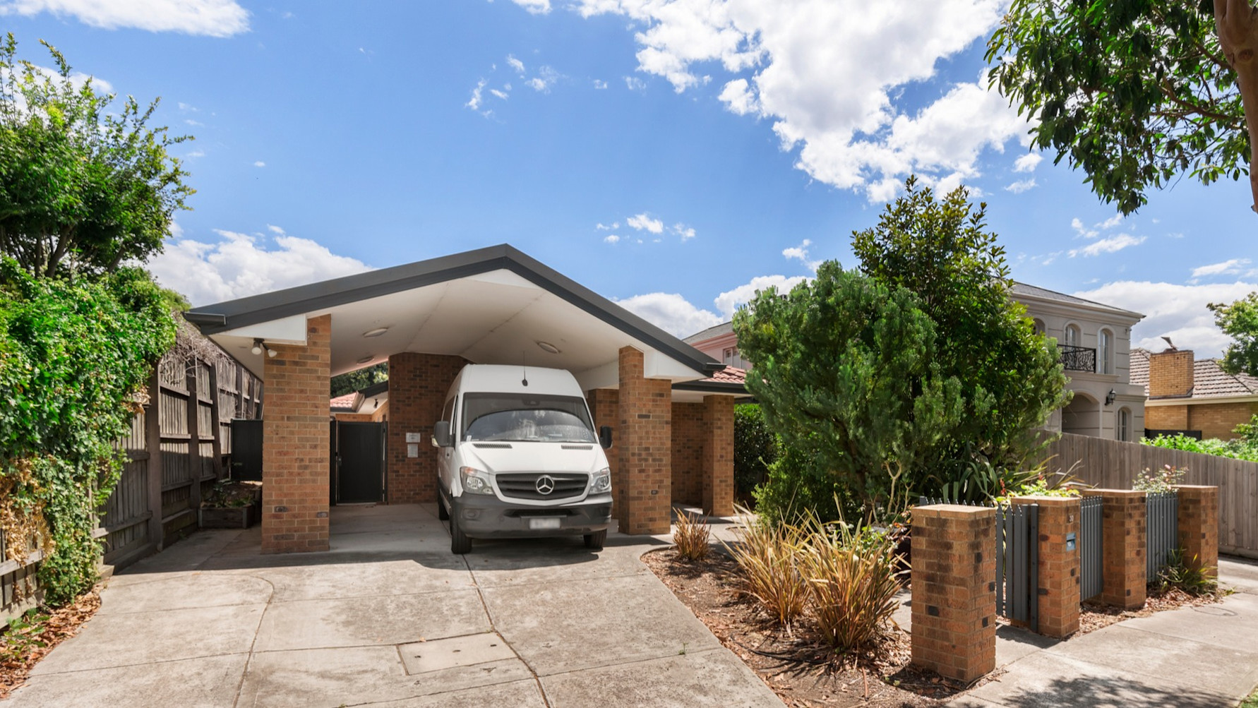 --Front of home with concrete driveway, carport, red bricks and trees. There is a white van in the front.--