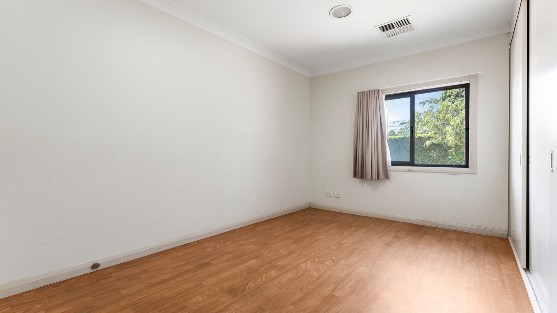 Vacant bedroom with hard wood flooring and window.