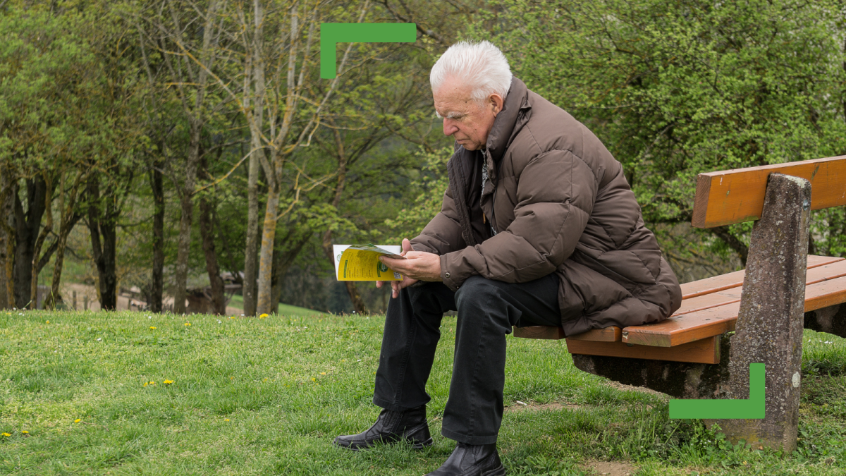 An older man sitting on a park bench holding a book.