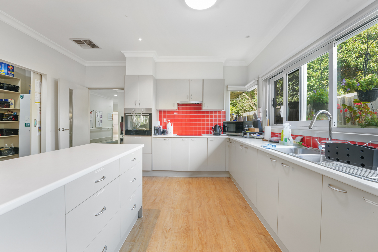 Spacious kitchen with island bench, red tiled splashback and large windows.